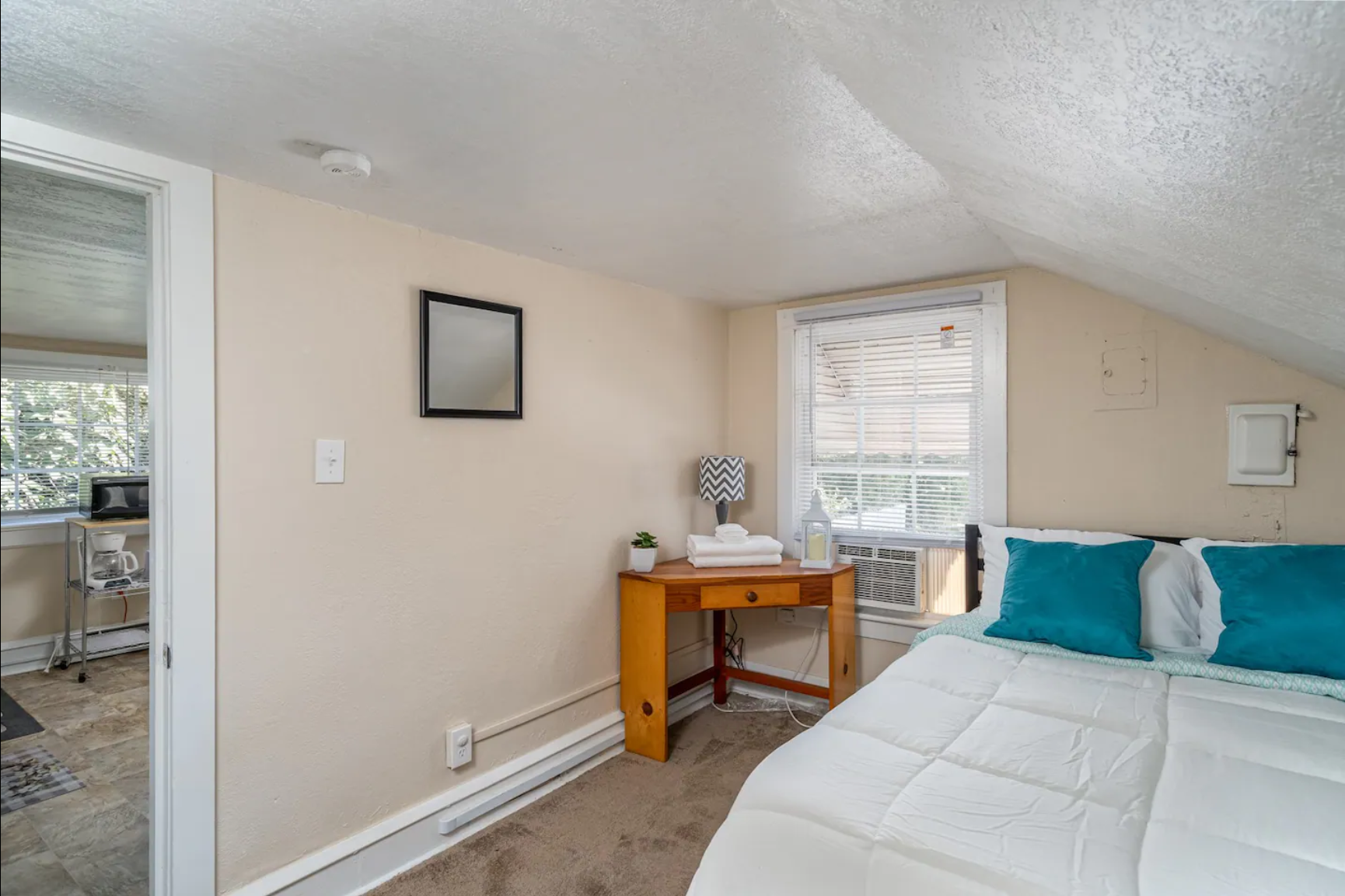 Sloped ceiling bedroom with white bed and teal accent pillows.